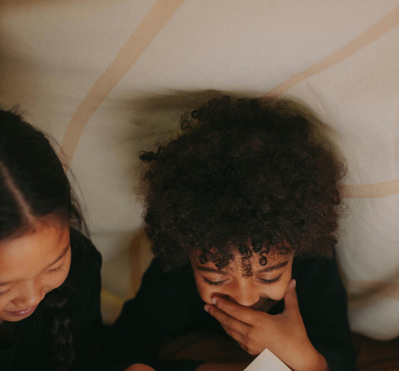 Two children reading a book together under a blanket fort