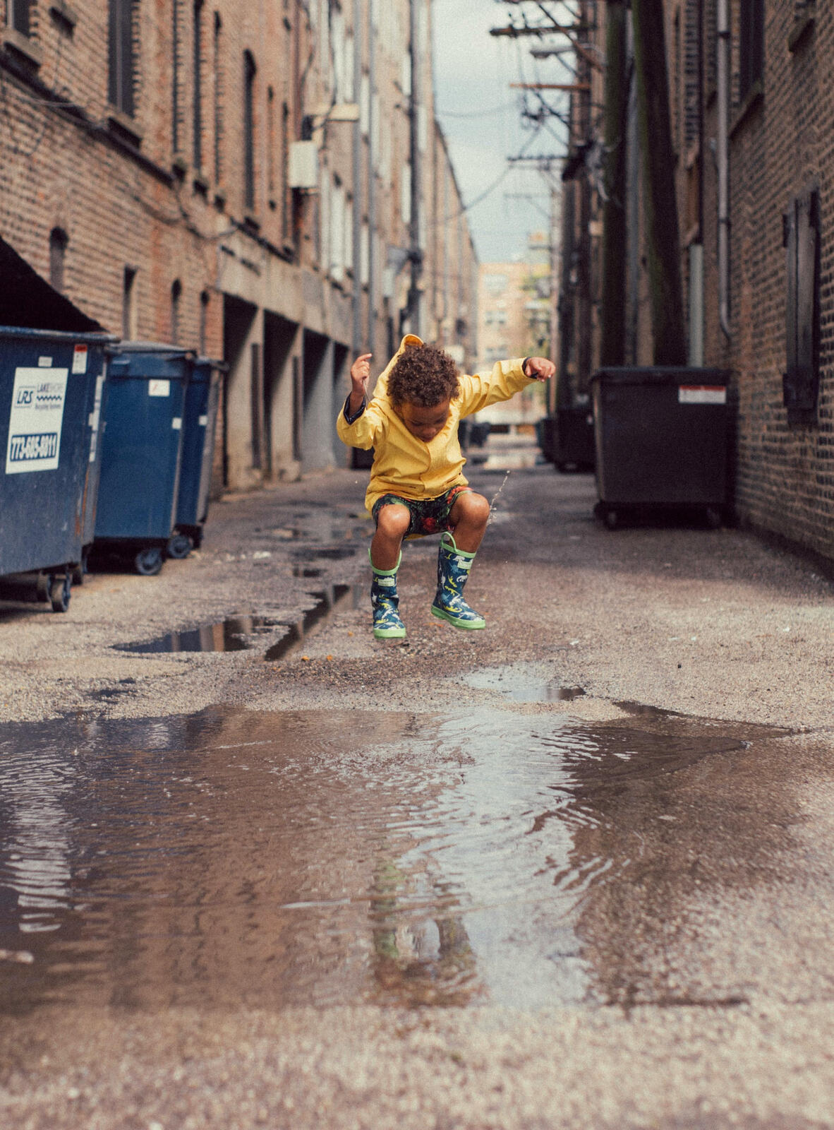 Child in a yellow raincoat and rubber boots jumping into a puddle