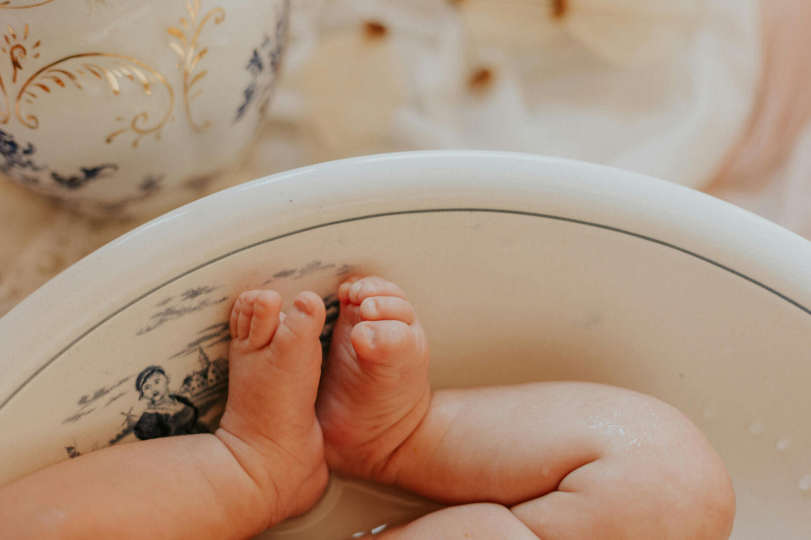 Newborn baby's feet resting in a vintage porcelain bath basin